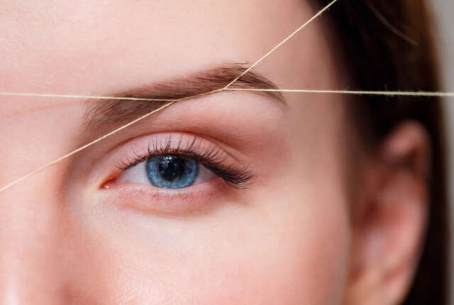 Cosmetologist plucks client eyebrows by thread. Close up Cosmetologist plucks client eyebrows by thread. Close up
