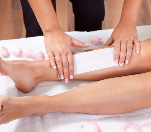 A beautician waxing a woman's legs on a towel Beautician doing depilation. Spa studio shot